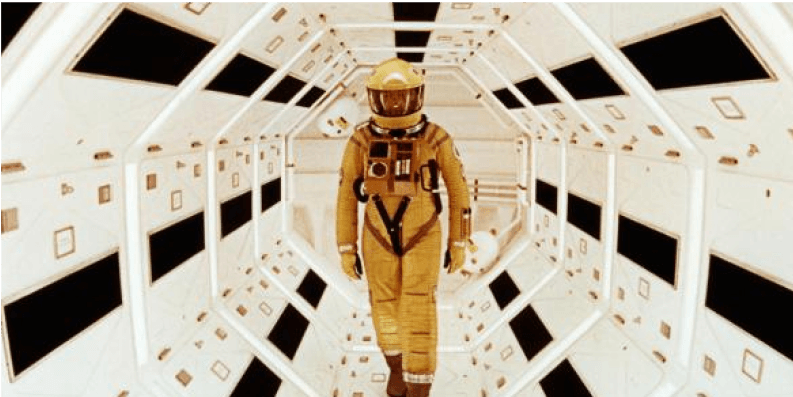 Astronaut walking inside the corridor of a spaceship or space station with white walls and black control panels.
