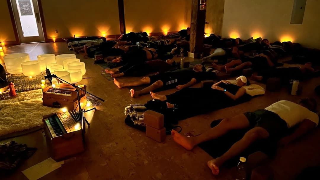 A candlelit Aloka sound bath: people resting on mats, crystal bowls glowing along the wall