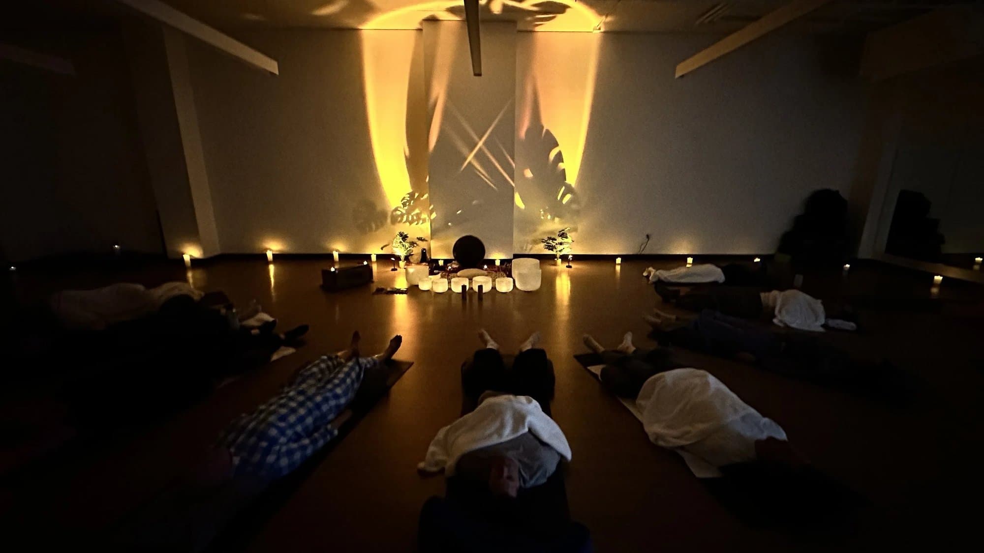 People resting on mats under blankets at an Aloka sound bath, crystal bowls glowing beneath a projected light pattern